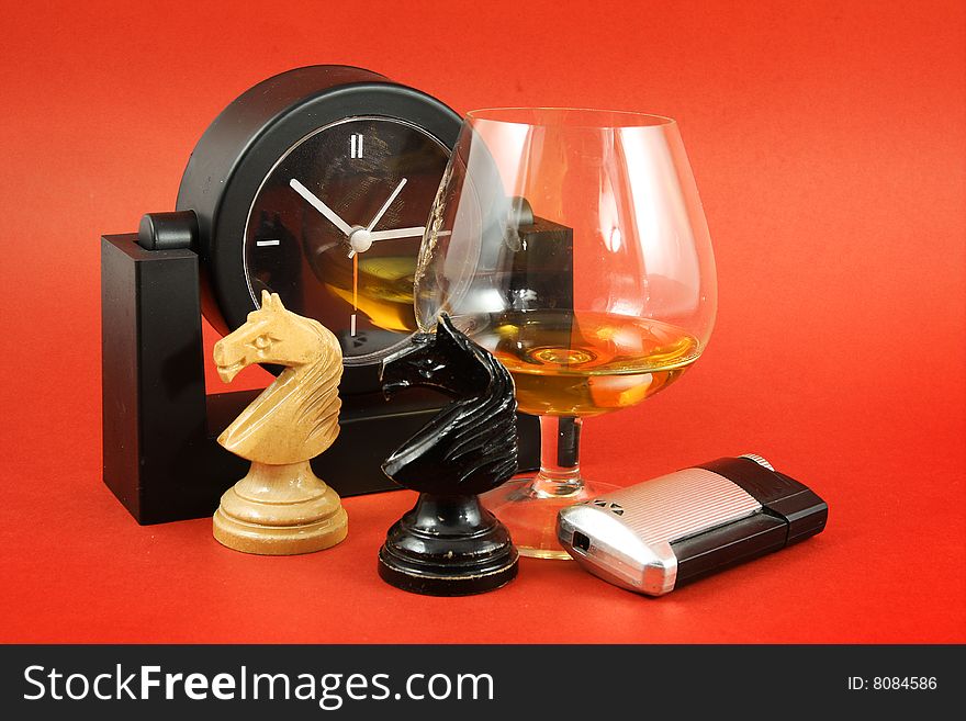 Still life with glass of brandy, chess and clock on red background