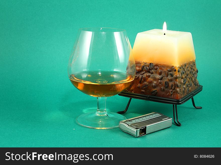 Still life with glass of cognac and burning   candle on green background. Still life with glass of cognac and burning   candle on green background