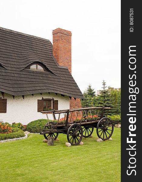 Cottage with thatched roof, old fashioned wooden carriage in foreground garden, Poland.