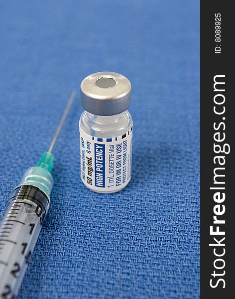 Small vial of medicine with a hypodermic needle on a surgical blue field. Small vial of medicine with a hypodermic needle on a surgical blue field.