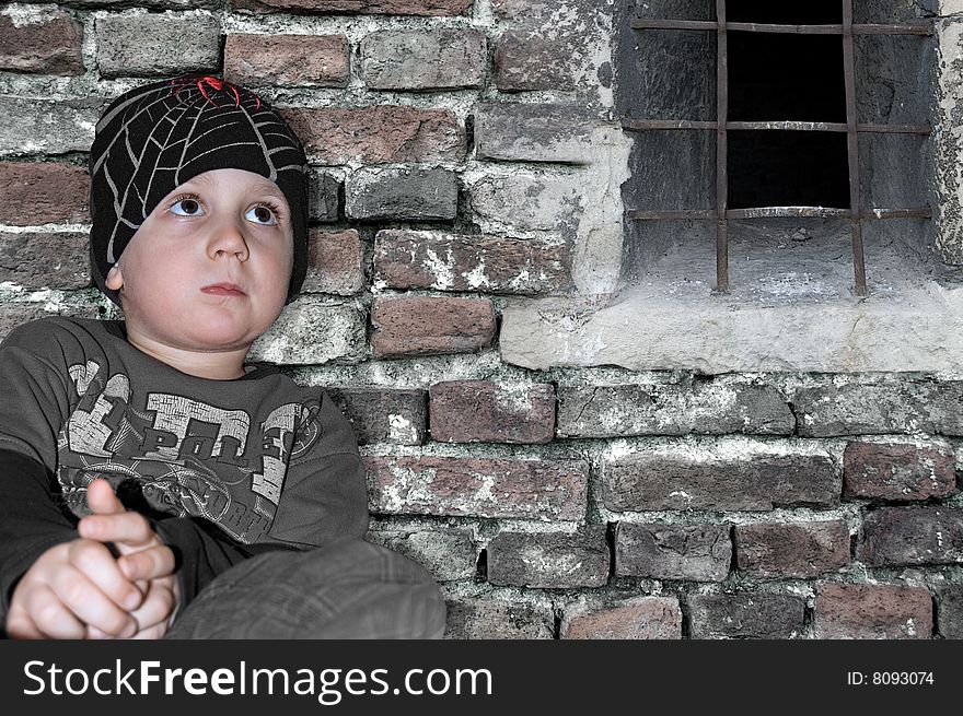 Little urban boy sitting in front of old brick wall