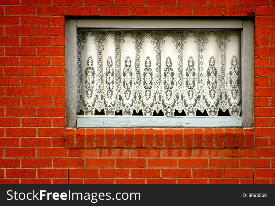 White lace drapery in a window in a brick wall. White lace drapery in a window in a brick wall.