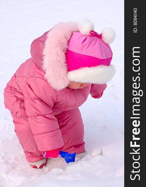 Pretty little girl with blue plastic toy rake in winter outerwear stay on snow-covered ground. Pretty little girl with blue plastic toy rake in winter outerwear stay on snow-covered ground.