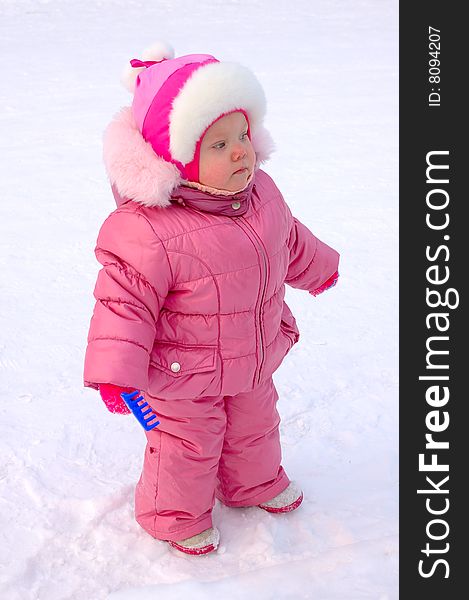 Pretty little girl with blue plastic toy rake in winter outerwear stay on snow-covered ground. Pretty little girl with blue plastic toy rake in winter outerwear stay on snow-covered ground.