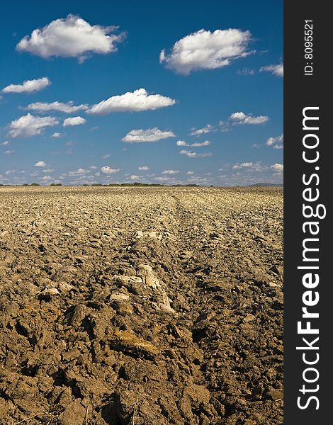 Rural landscape with the ploughed field and the dark blue sky with white clouds