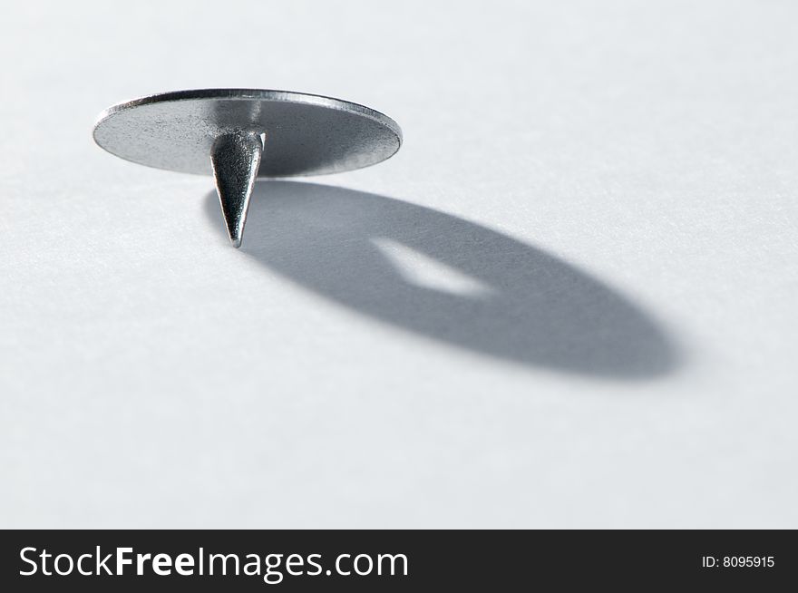 Old-style steel pushpin on white paper casting a shadow. Old-style steel pushpin on white paper casting a shadow