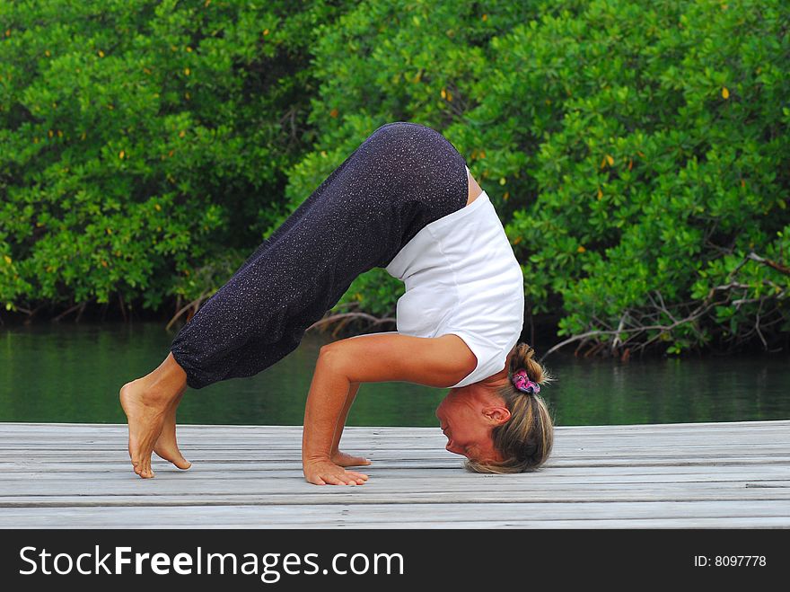 Woman doing yoga on wooden dock with green mangrove behind  her.