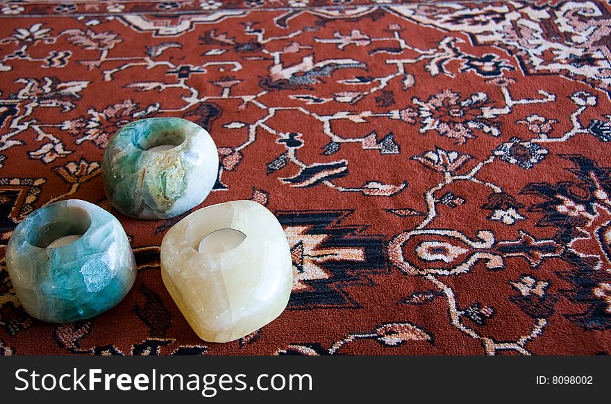 Three stone candle holders with three unlit candles in them on a decorative cloth