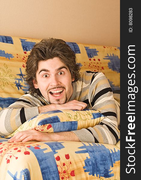 Young dark haired caucasian man in striped sweater lying on country style sofa ��� laughing. Young dark haired caucasian man in striped sweater lying on country style sofa ��� laughing