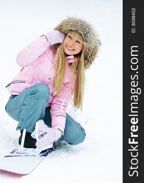 Beautiful young woman putting on a snowboard on the mountain