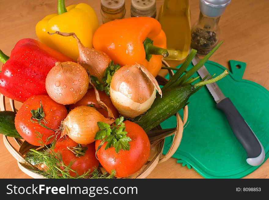 Crude vegetables in a basket, a chopping board, a knife, olive oil and spices. Crude vegetables in a basket, a chopping board, a knife, olive oil and spices.