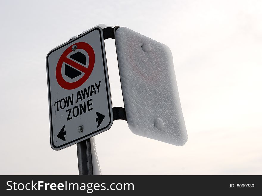 A tow away zone sign half frozen by mist in the cold of winter.