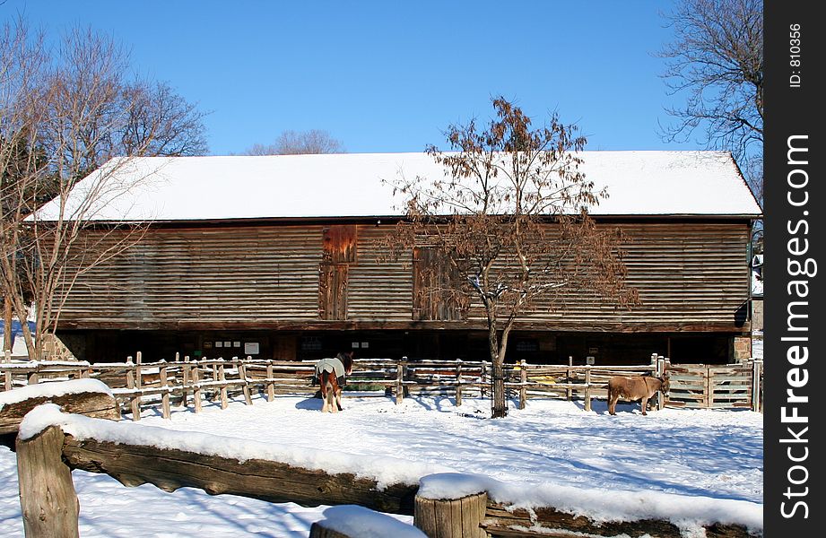 A barn in covered with snow. Donkey and horse in the background. A barn in covered with snow. Donkey and horse in the background