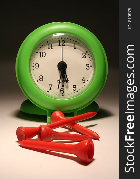 Green clock showing home time, along with some red golf tees. Green clock showing home time, along with some red golf tees