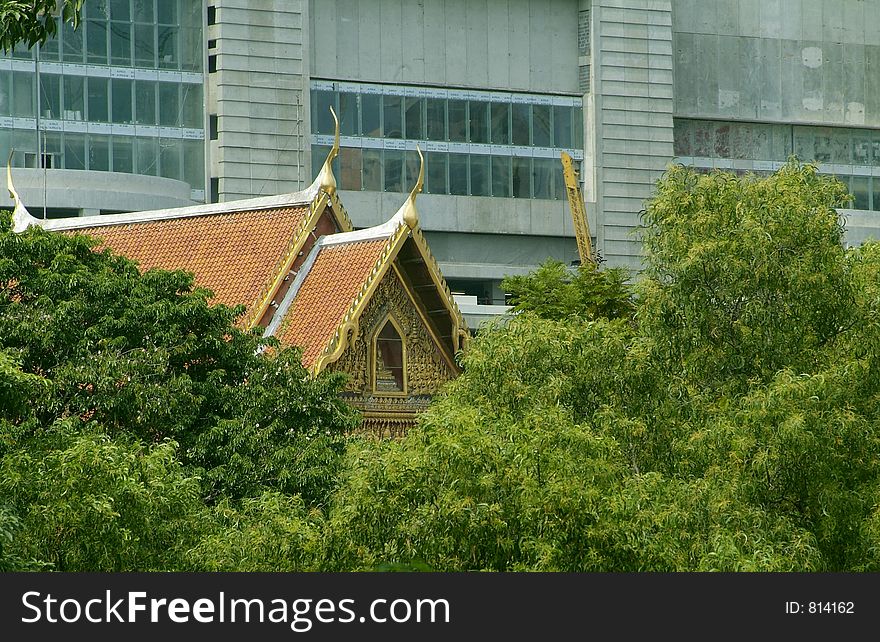 Traditional style Buddhist temple among trees in the city of Bangkok, Thailand, with a modern style shopping mall in the background. Traditional style Buddhist temple among trees in the city of Bangkok, Thailand, with a modern style shopping mall in the background