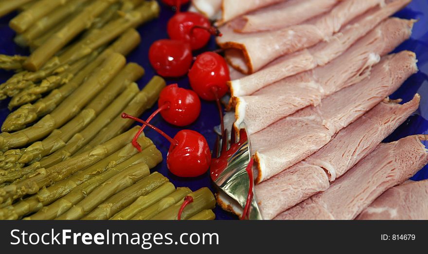 Asparagus, cherries and sliced ham on a deep blue plate, ready to be served at a party. Asparagus, cherries and sliced ham on a deep blue plate, ready to be served at a party