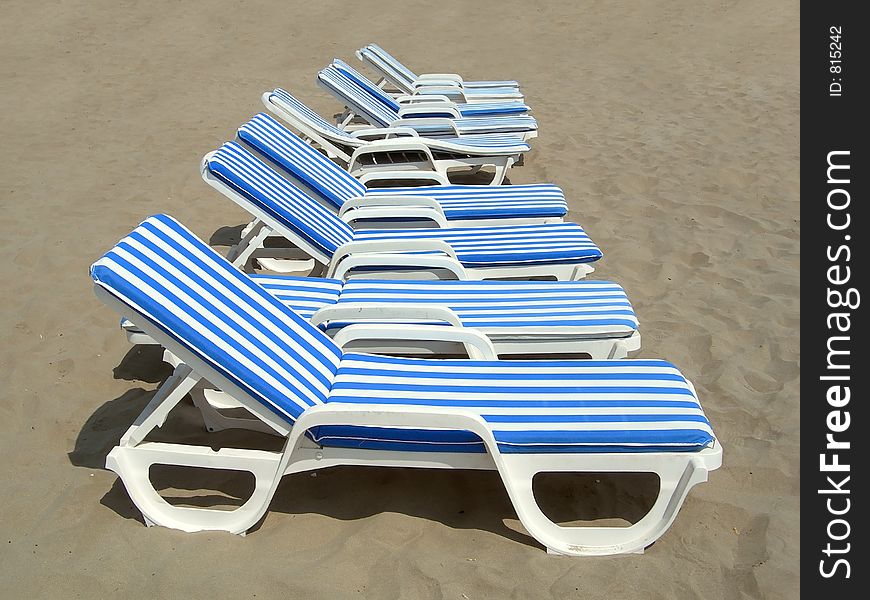 File of six white and blue beach-chairs in the sand of a beach. File of six white and blue beach-chairs in the sand of a beach