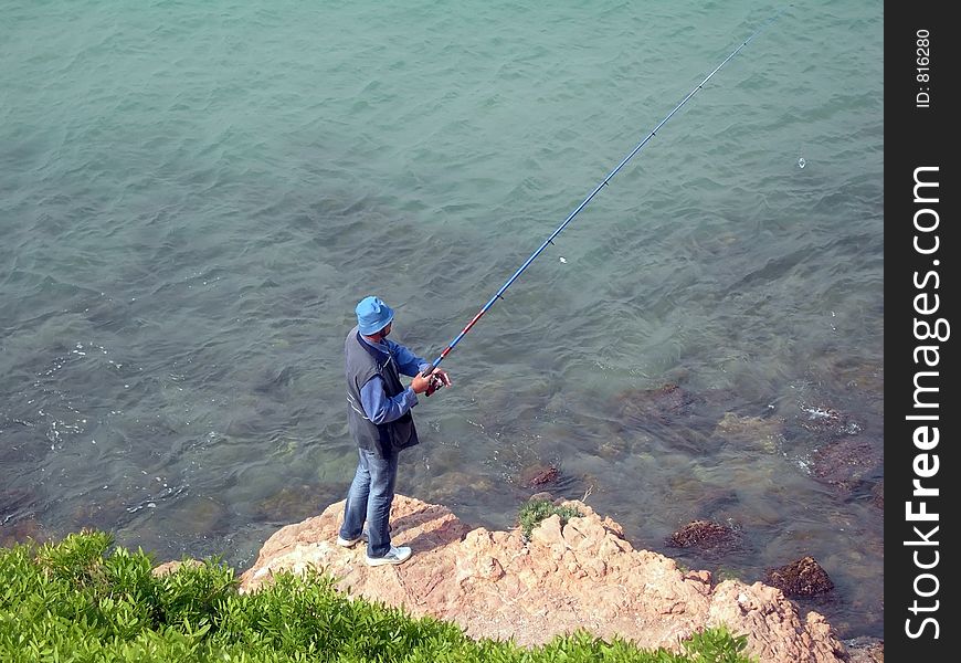 Man in blue fishing on a rock. Man in blue fishing on a rock