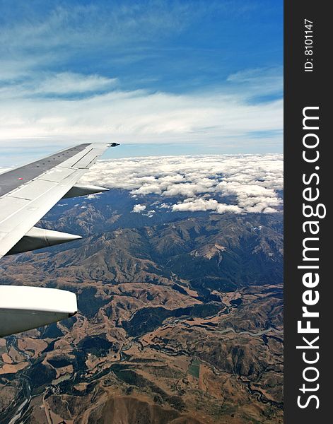 Airplane wing over mountain terrain with cloudy sky. Airplane wing over mountain terrain with cloudy sky