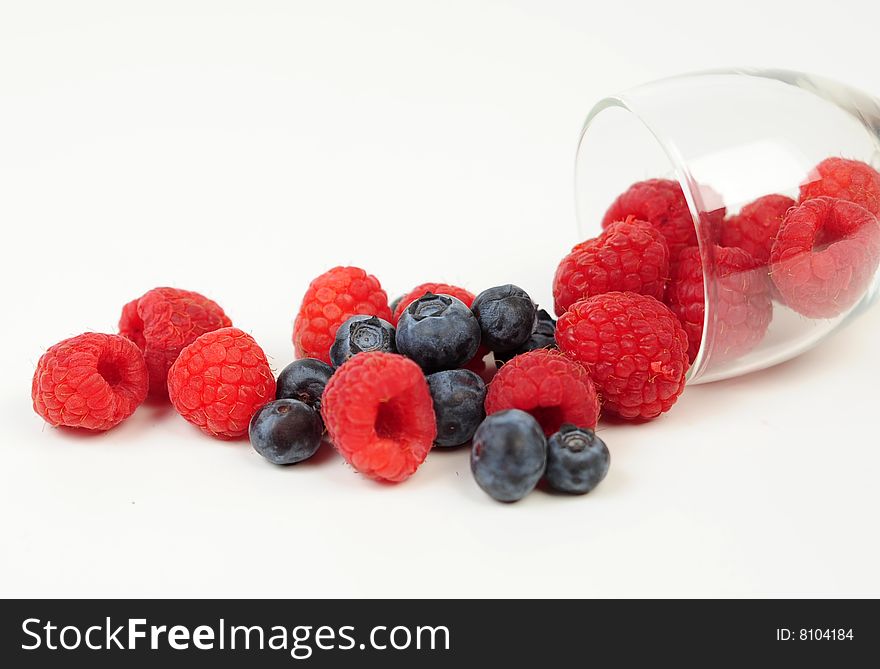 A clear glass pouring out a mix of yummy raspberries and blueberries. A clear glass pouring out a mix of yummy raspberries and blueberries.