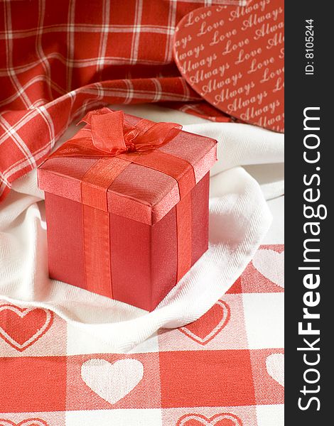 Red Valentines gift box on table cloth with red hearts. Red Valentines gift box on table cloth with red hearts