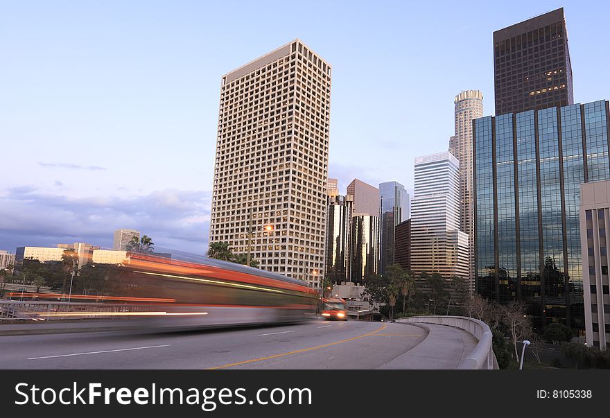 Two buses traveling through Los Angeles just after sunset