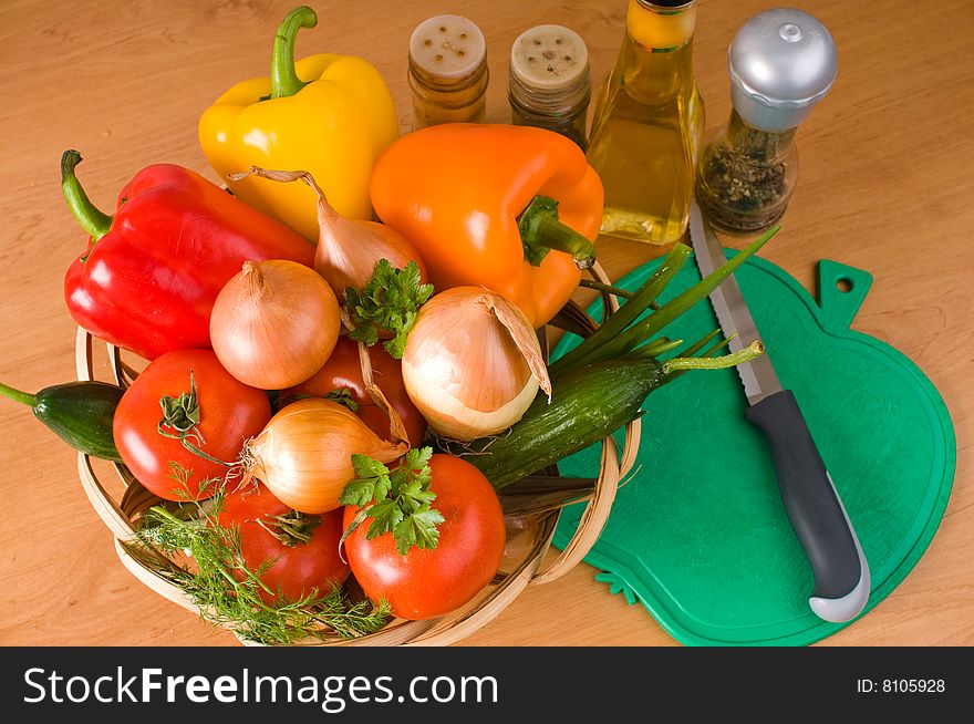 Crude vegetables in a basket, a chopping board, a knife, olive oil and spices. Crude vegetables in a basket, a chopping board, a knife, olive oil and spices.