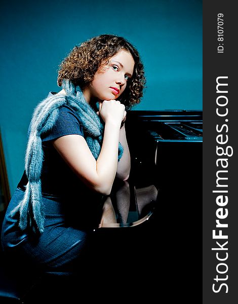 Pretty young dark haired girl sitting near piano with hands ctossed in front looking forward with fur scarf and reflections on cover isolated. Pretty young dark haired girl sitting near piano with hands ctossed in front looking forward with fur scarf and reflections on cover isolated