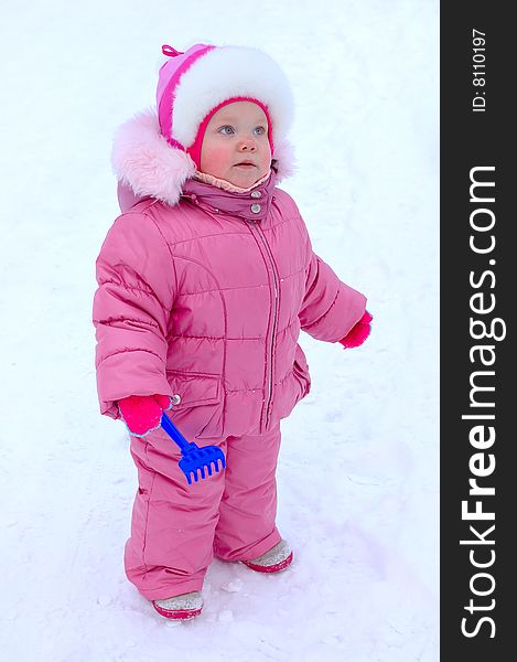 Pretty little girl with blue plastic toy rake in winter outerwear stay on snow-covered ground. Pretty little girl with blue plastic toy rake in winter outerwear stay on snow-covered ground.