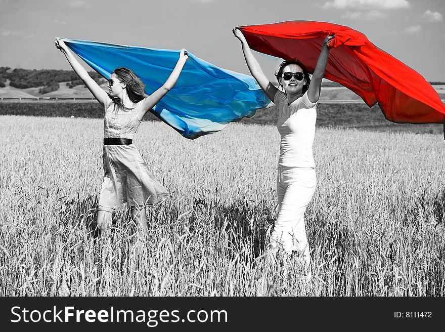 Two young beautiful woman running on the field with a red and blue scarfs