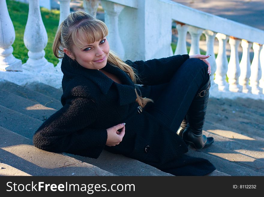 Beautiful young woman lies on the stairs in a black overcoat