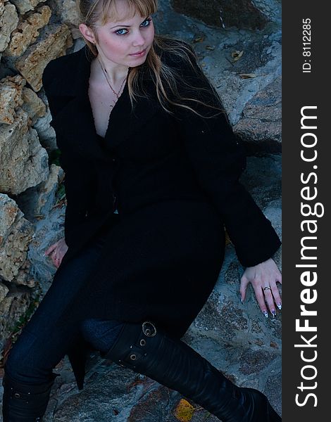 Beautiful young woman lies on the stairs in a black overcoat