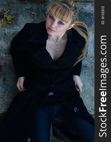 Beautiful young woman lies on the stairs in a black overcoat