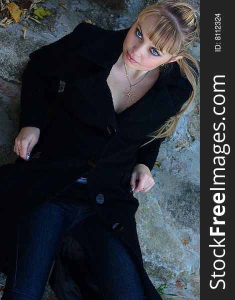 Beautiful young woman lies on the stairs in a black overcoat