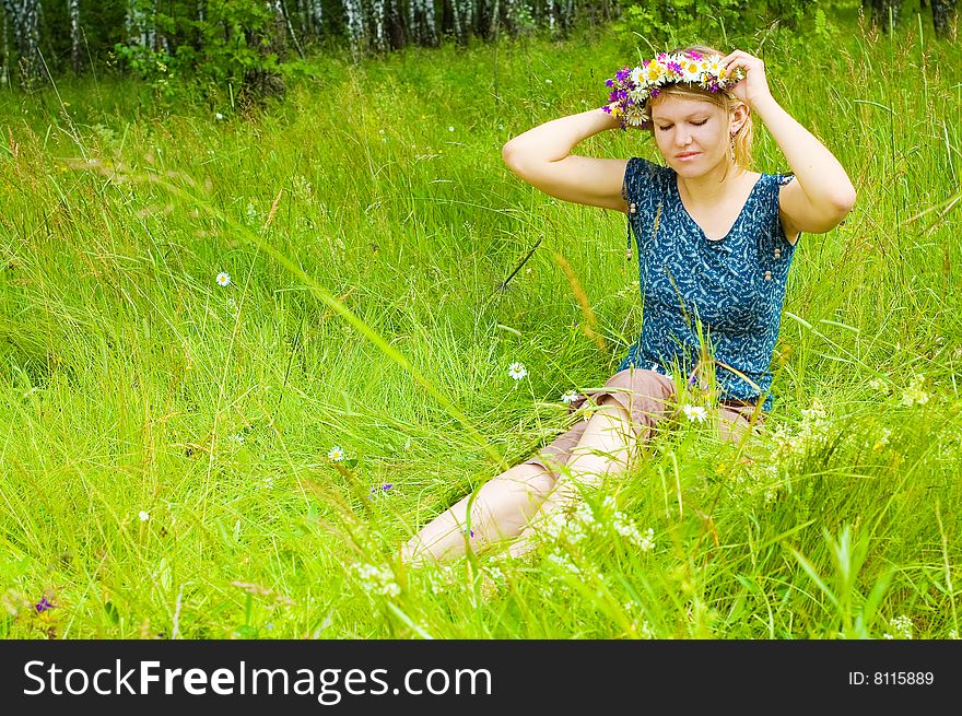 Young woman twining a  wreath on the meadow
