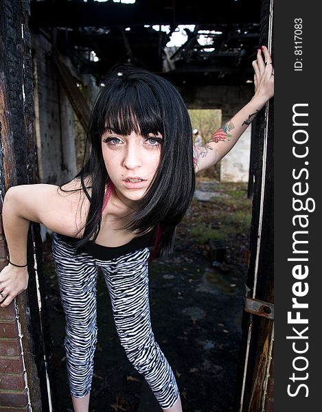 Pretty young woman with a left arm tattoo standing in a doorway of an abandoned building. Pretty young woman with a left arm tattoo standing in a doorway of an abandoned building
