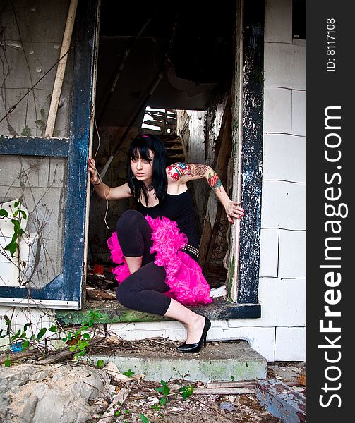 Pretty young woman with a left arm tattoo kneeling in a doorway of an abandoned building. Pretty young woman with a left arm tattoo kneeling in a doorway of an abandoned building