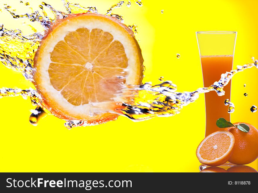 View of piece of orange getting splashed  and  glass of juice on back. View of piece of orange getting splashed  and  glass of juice on back