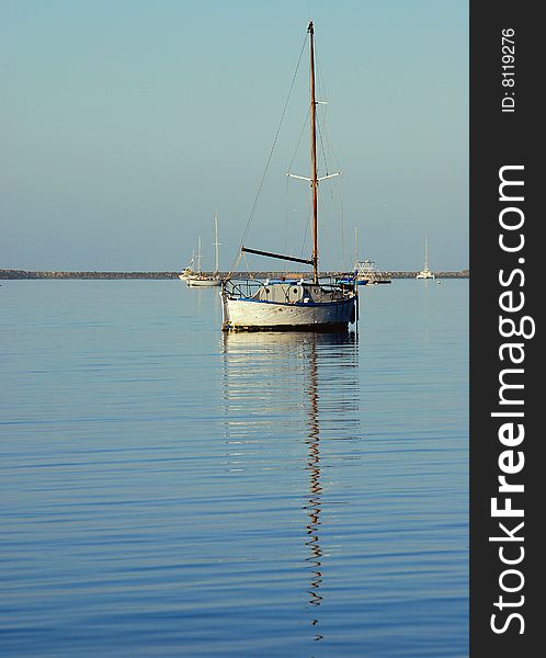 Small wooden sloop and reflection in a calm anchorage on a still day. Small wooden sloop and reflection in a calm anchorage on a still day.