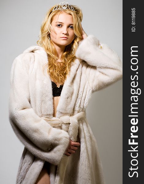 Portrait of young woman in white fur coat and black bra on grey
