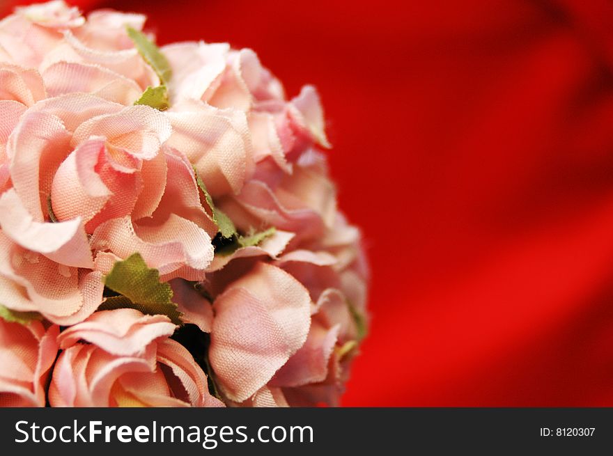 Fake pink flowers against red silky  background with a space for a text. Fake pink flowers against red silky  background with a space for a text