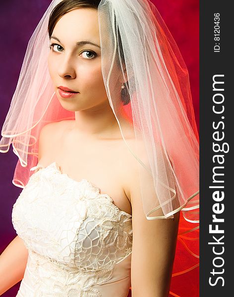 Studio portrait of a young bride wearing a veil and a white wedding dress against red background. Studio portrait of a young bride wearing a veil and a white wedding dress against red background