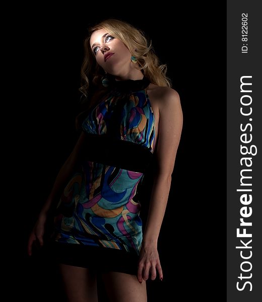 Beautiful blonde young lady in multicolored dress on black background