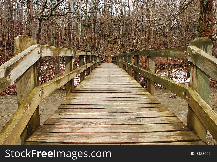 This is a shot of a wooded bridge walkway over a river. A little bit of the river can be seen on either side of the bridge. Woods can be seen on the opposite side of the walkway. This is a shot of a wooded bridge walkway over a river. A little bit of the river can be seen on either side of the bridge. Woods can be seen on the opposite side of the walkway.