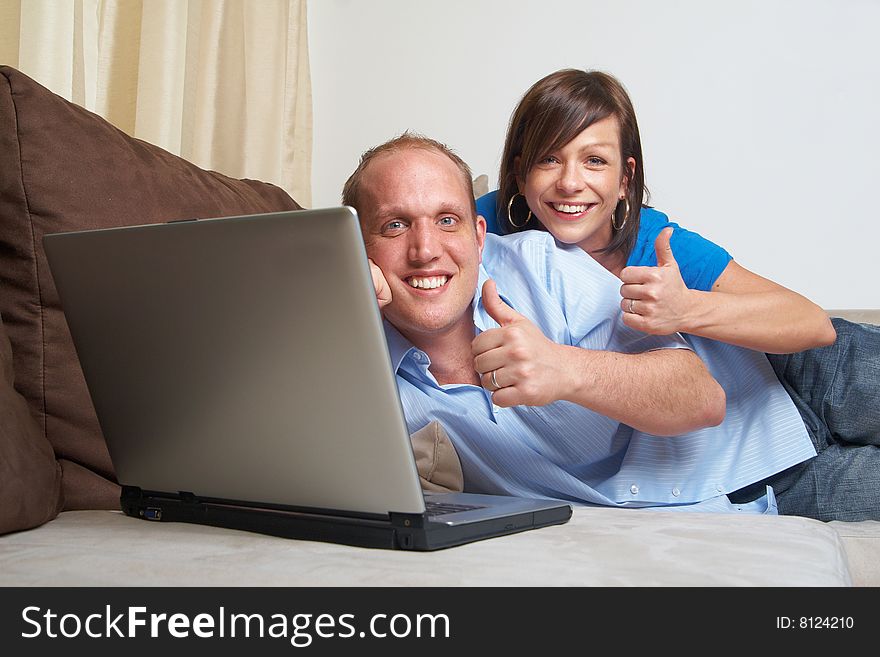 Young couple on the couch at home looking at the laptop! They both give a thumbs up sign!