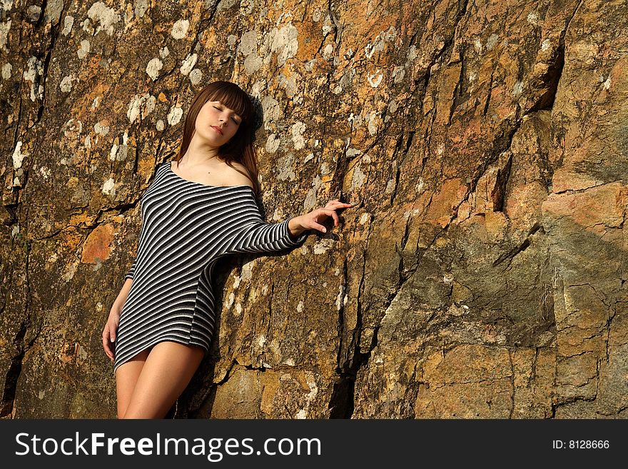 Young woman on the rock, in stripy dress. Give out warmth