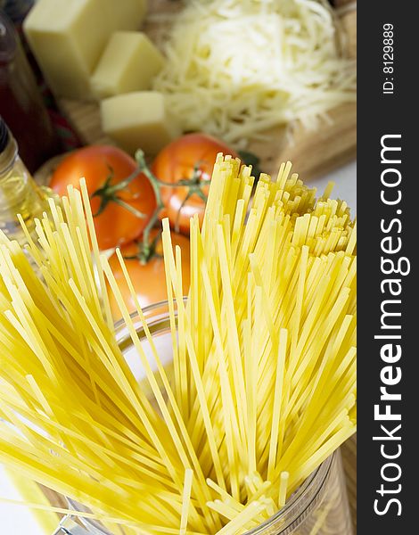 Overhead shot of ready for cooking spaghetti in glass container with tomatoes and cheese in the background. Overhead shot of ready for cooking spaghetti in glass container with tomatoes and cheese in the background