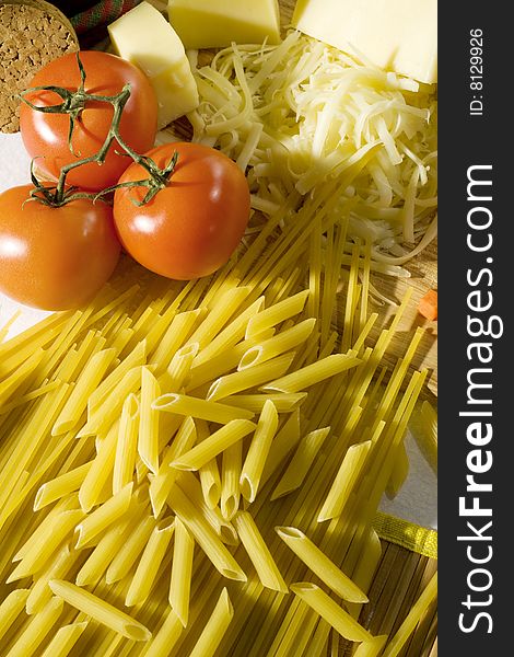 Overhead shot of raw spaghetti and macaroni next to a tomatoes and grated cheese