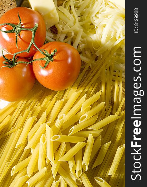 Overhead shot of raw macaroni and spaghetti next to a grated cheese and tomatoes