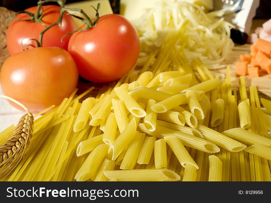 Overhead shot of raw spaghetti and macaroni next to a tomatoes and grated cheese